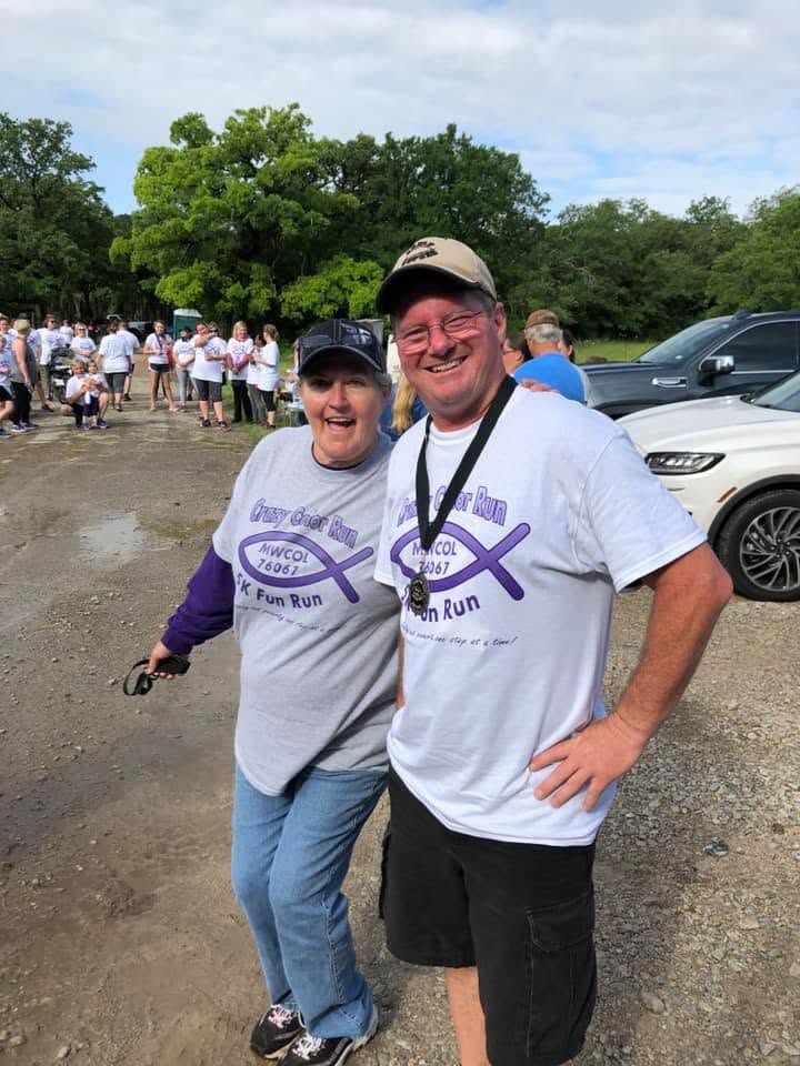 Two people smiling outdoors in matching fun run shirts.