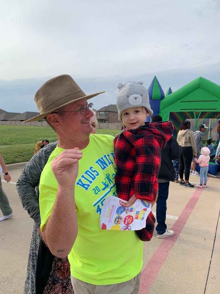 An adult holding a young child at an outdoor gathering.